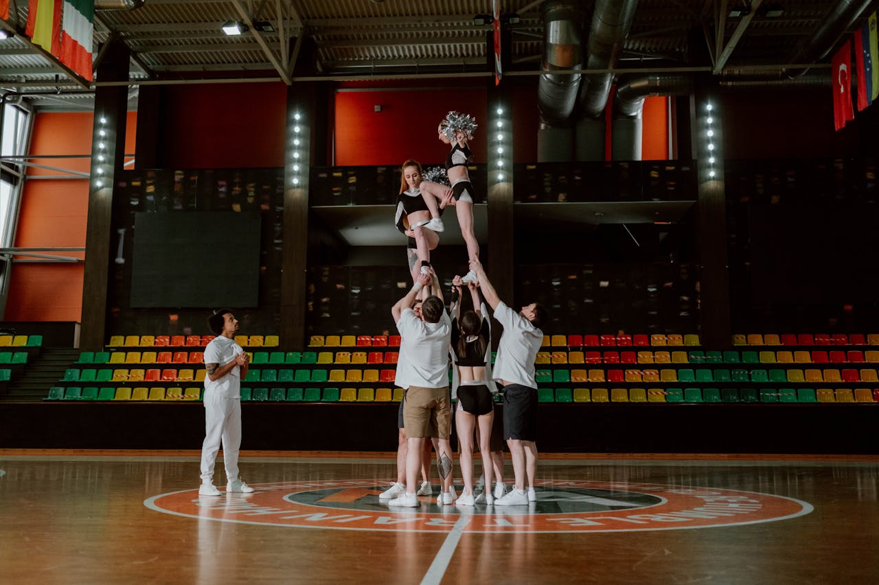 Cheerleading team performing a complex stunt indoors in a brightly lit arena.