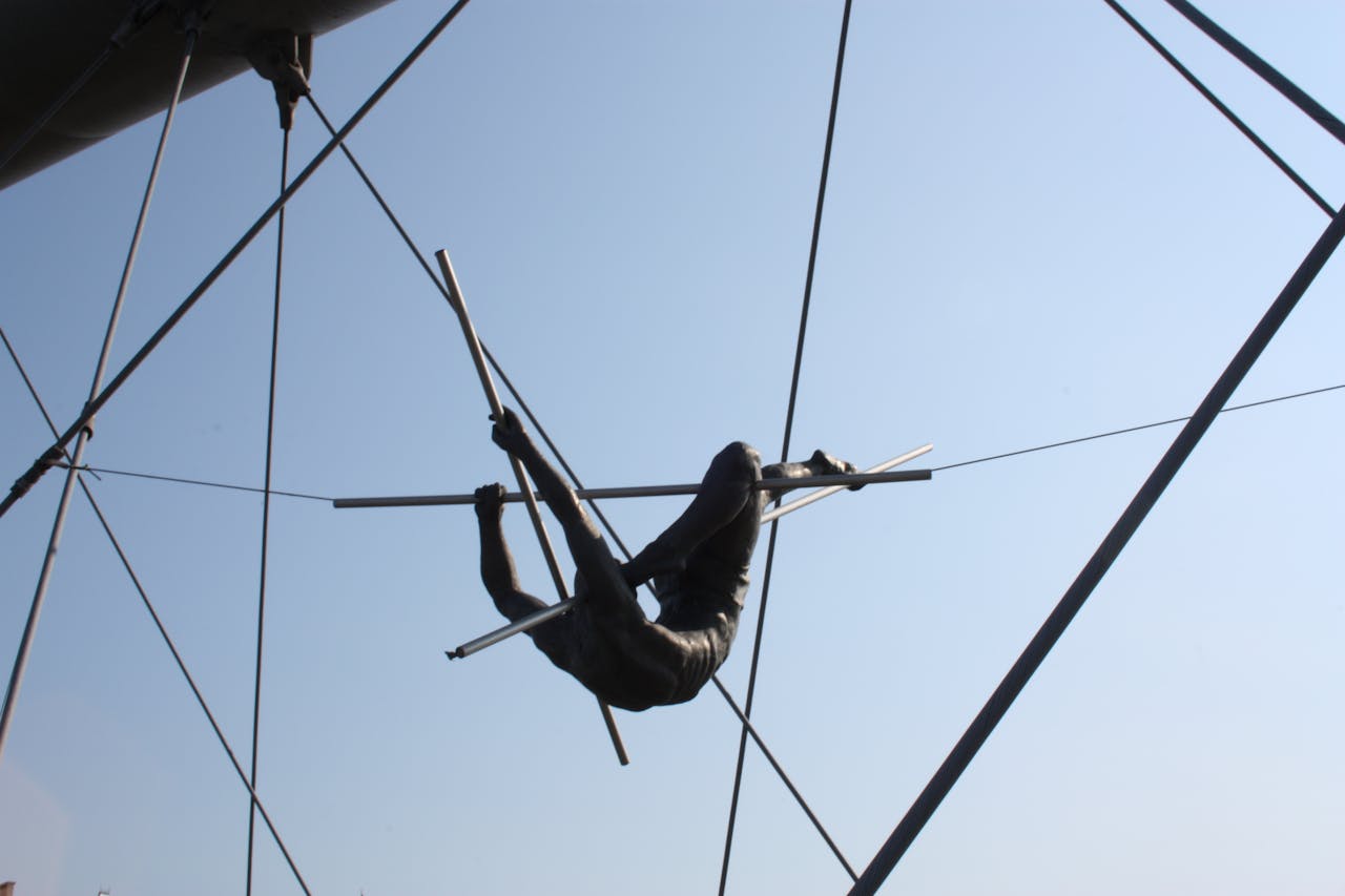 Silhouette of an acrobat performing on a trapeze with a clear blue sky background.
